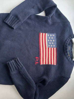 Mörkblå stickad tröja Polo Ralph Lauren - Nu säljer jag min trendiga Ralph Lauren tröja, då det tyvärr har blivit för liten. Det är en Mörkblå stickad tröja från Polo Ralph Lauren med amerikansk flagga och RL-broderi på bröstet. Perfekt för dig som gillar klassisk preppy stil!! NYPRIS: 4965kr 