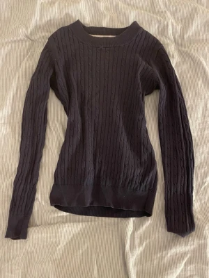 Mörkblå kabelstickad tröja - Snygg mörkblå kabelstickad tröja med rund halsringning och långa ärmar. Tröjan har ribbade muddar vid ärmslut och nederkant, vilket ger en klassisk och stilren look. Perfekt att matcha med jeans eller kjol.❤️