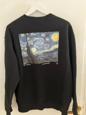 Svart sweatshirt med Starry Night-tryck - Cool svart sweatshirt med tryck av Van Goghs 'Starry Night' på ryggen och texten 'Vincent 1853' fram. Tröjan har rund hals, långa ärmar och ribbade muddar. Perfekt för dig som gillar konst och vill ha en unik stil.