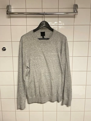 Ljusgrå basic stickad tröja H&M - En enkel och stilren ljusgrå stickad tröja från H&M. Tröjan har rund halsringning, långa ärmar och ribbade muddar vid ärmslut och nederkant. Tillverkad i mjukt material som passar perfekt för lager på lager. Klassisk modell som funkar till allt.