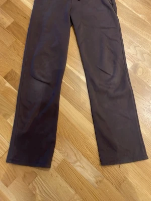 Bruna mjukisbyxor med raka ben - Mörkbruna mjukisbyxor med raka ben och resår i midjan. Byxorna har en enkel och clean design utan synliga loggor eller detaljer. Har 2 fikor där fram och inga där bak. Materialet känns mjukt och skönt mot huden.