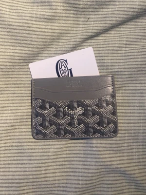 Grå korthållare i läder - Snyggt och stilrent kortfodral  i grått med klassiskt mönster och logga framtill. Tillverkat i läder och canvas, perfekt för kort och ID. Kommer med originalask och kort. En riktig statement-accessoar för dig som gillar lyxiga detaljer.