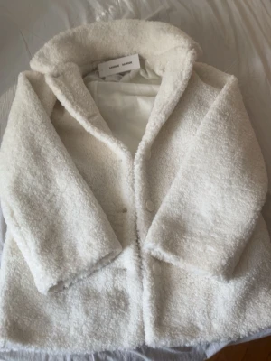 Vit teddyjacka från Samsøe Samsøe - Supermjuk och fluffig teddyjacka i vitt, Jackan har bred krage, knäppning framtill med stora knappar och en boxig, avslappnad passform. Perfekt för att hålla sig varm och stilsäker under kyliga dagar. (Pris kan diskuteras )