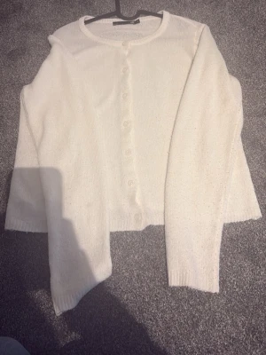 Vit kofta från 157 med knappar - Klassisk vit kofta från 157 med rund halsringning och knäppning framtill. Koftan har långa ärmar och ribbade muddar vid ärmslut och nederkant. Perfekt att slänga över en topp för en enkel och clean look.