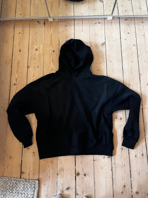 Acne Studios Hoodie - Säljer en svart hoodie från Acne Studios med tryck på ryggen där det står 'Acne Studios STOCKHOLM 1996'. Hoodien har en klassisk passform, huva och ribbade muddar. Perfekt för en avslappnad och stilren look.