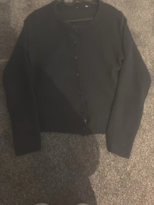 Svart kofta från 157 med knappar - En enkel och stilren svart kofta från 157 med rund halsringning och knäppning framtill. Koftan har långa ärmar och är tillverkad i ett mjukt material som passar perfekt till lager på lager. Snygg att matcha med jeans eller kjol.