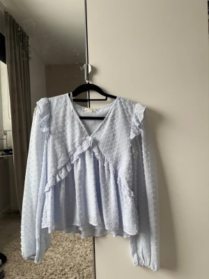 Ljusblå volangblus med prickar - Supersöt ljusblå blus med volanger och strukturprickar. Blusen har v-ringning, långa puffärmar med resår vid ärmslut och ett luftigt, flowy material. Perfekt för en trendig look.        PRIS KAN DISKUTERAS !
