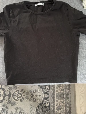 Svart croppad t-shirt - En enkel svart croppad t-shirt med rund hals. T-shirten har korta ärmar och är tillverkad i mjuk bomull, perfekt för en avslappnad och stilren look.