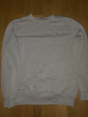 Vit sweatshirt från Moncler - Klassisk vit sweatshirt från Moncler med rund halsringning och diskret Moncler-logga på bröstet. Tröjan har långa ärmar och ribbade muddar vid ärmslut och nederkant. Perfekt för en clean och stilren look.