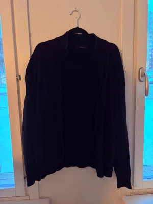 Svart öppen kofta - En enkel svart öppen kofta med lång ärm och avslappnad passform. Perfekt att slänga över en t-shirt eller topp för en stilren look. Tillverkad i mjukt material som känns skönt mot huden.