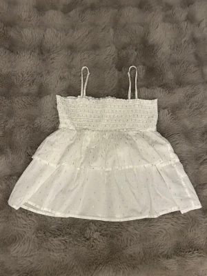 Vit volangig linnetopp med smock - Vit topp med glittriga gulddetaljer. Storlek 158/164