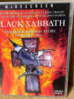 The Black Sabbath Story Vol. 2 DVD - En DVD med titeln 'The Black Sabbath Story Volume Two' som innehåller liveframträdanden och intervjuer med bandet Black Sabbath. Omslaget är svart och rött med en ikonisk demonillustration och text i vitt och gult.