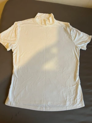 Två polotoppar i vitt och svart - Säljer två stilrena polotoppar, en i vitt och en i svart. Båda har hög krage och korta ärmar, perfekta att matcha med jeans eller kjol. Materialet känns mjukt och stretchigt, troligen polyester eller bomullsmix. Passformen är normal och de är enkla att styla.