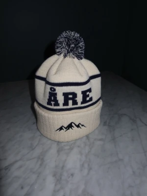 Åre mössa  - Riktigt fräsch Åre mössa från SkiStyle UF✅. Framsidan har ÅRE-text och ett broderat bergmotiv och färg cream. Stickad i mjukt material, otrolig kvalitet och perfekt för kalla dagar, skriv vid frågor eller funderingar! 