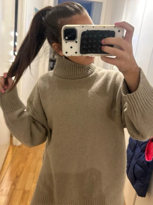 Beige stickad polotröja - Mysig beige stickad polotröja med oversized passform och breda ribbade muddar vid ärmslut och nederkant. Hög polokrage som ger extra värme. Perfekt för lager-på-lager och enkel att styla till olika outfits.