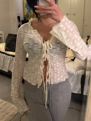 Vit spetsblus med snörning - Säljer en superfin vit blus i spets med blommigt mönster. Toppen har långa ärmar, volangkant och snörning framtill som ger en romantisk vibe. Perfekt att styla med jeans eller kjol för en trendig look.