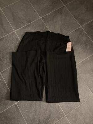 Svarta ribbade leggings från Nelly - TRYCK EJ PÅ KÖP DIREKT!!Säljer ett par svarta leggings från Nelly med ribbad struktur och hög midja. De har en rak passform och är tillverkade i ett stretchigt material som sitter skönt. Perfekta för en trendig och avslappnad look.