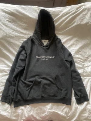Mörkgrå hoodie från Gosha Rubchinskiy - Mörkgrå hoodie med vit rysk text på bröstet och stor känguruficka framtill. Klassisk passform med ribbade muddar och en rejäl huva. Tillverkad i mjukt bomullsmaterial som känns skönt mot huden. Perfekt för dig som gillar streetwear och vill sticka ut.