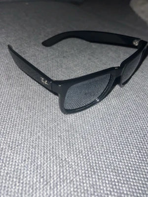 Svarta Ray-Ban solglasögon - Snygga svarta solglasögon från Ray-Ban med klassisk wayfarer-form. Bågarna är i plast och har Ray-Ban-loggan på sidan. Perfekta för dig som vill ha en tidlös och stilren look. Är lite skrapad där framme jätte litet.