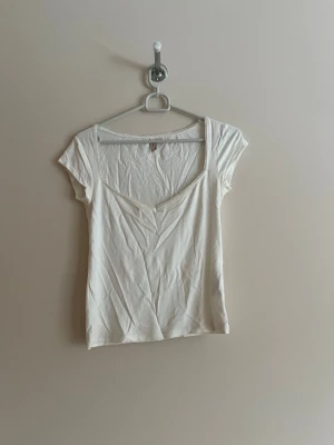 Vit topp med spetskant - Söt vit topp med v-ringning och spetskant runt halsen. Kortärmad och i mjukt bomullsmaterial, perfekt till jeans eller kjol. Enkel och stilren design som passar till många olika looks.