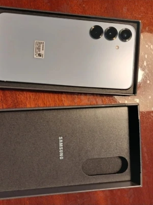 Samsung Galaxy S25+ silver - Samsung Galaxy S25+ i elegant silverfärg med stilren design och rundade hörn. Baksidan har tre kameror i rad och en minimalistisk look. Telefonen levereras i originalkartong med Samsung-logga. Perfekt för dig som vill ha en modern Android-mobil.