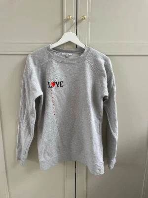 Grå sweatshirt från Ganni - En perfekt grå sweatshirt från Ganni med med detalj på bröstet. Tröjan är använd ett fåtal gånger. Det är strl. XS men passar mig som är S-M vanligtvis. 