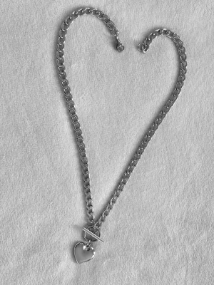 Silverfärgat halsband med hjärthänge - Snyggt halsband i silverfärgad metall med en chunky kedja och ett hjärtformat hänge. Halsbandet har ett toggle-lås som ger en trendig touch. Perfekt accessoar för att lyfta din outfit med en stilren och modern känsla.