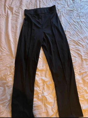 Svarta kostymbyxor med pressveck - Säljer ett par svarta kostymbyxor med raka ben och markerade pressveck framtill. Byxorna har hög midja och bred linning för en snygg siluett. Perfekta att styla med en skjorta eller crop top.