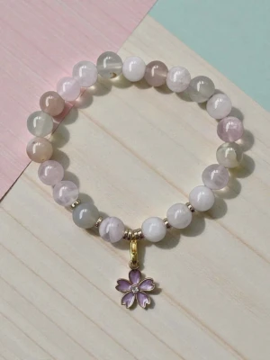 Armband med rosenkvarts kristaller & Agat kristaller - Sött armband med runda pärlor i pastellfärger som rosa, vitt och ljusgrått. Armbandet har en liten lila blomma som hänge i metall med gulddetaljer. Perfekt accessoar för dig som gillar en mjuk och feminin stil.