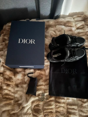 Svarta Dior B30 sneakers - Säljer ett par svarta Dior B30 sneakers med vita detaljer och reflekterande inslag. Skorna har en sportig design med mesh och läderpaneler, samt tydlig Dior-logga på plösen. Kommer med originalkartong och dustbag.