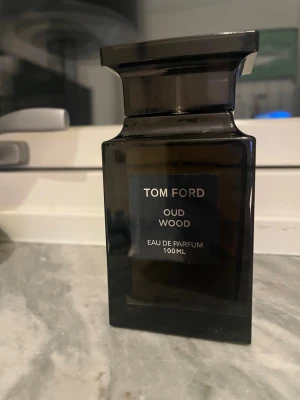 Tom Ford Oud Wood Eau de Parfum 100ml - Exklusiv parfym från Tom Ford i doften Oud Wood. Flaskan är mörkbrun och har en elegant, fyrkantig form med svart etikett och silvertext. Innehåller 100 ml Eau de Parfum. Perfekt för dig som gillar lyxiga och träiga dofter. Boxen är borta
