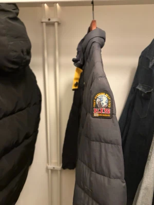 Parajumper jacka - Snygg mörkgrå pufferjacka från Parajumpers med gul detalj vid kragen och klassisk patch på ärmen. Jackan har hög krage, dragkedja framtill och quiltad design som ger en modern look. Perfekt för kalla vinterdagar. Skriv vid funderingar 