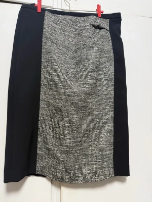 Svart och grå kortkjol med mönster från weekend maxmara - Stilren kortkjol med svart bas och gråmelerat parti framtill. Kjolen har rak passform och är perfekt för dig som gillar en klassisk look med en twist. Inga synliga detaljer som knappar eller dragkedja. Passar till många olika outfits.