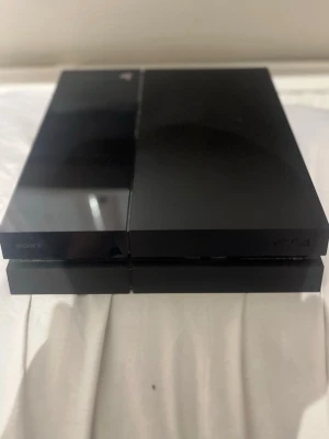 Sony PlayStation 4 spelkonsol svart - PlayStation 4 spelkonsol från Sony i stilren svart färg. Konsolen har en kantig, rektangulär design med både matt och blank finish. Perfekt för gaming och underhållning, tillverkad i plast med klassisk PS4-look.