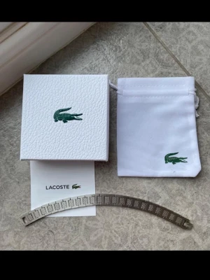 Silverfärgat armband från Lacoste - Snyggt armband i silverfärgad metall från Lacoste. Den är 21cm men kanenkelt justeras kan också hjälpa med det😊