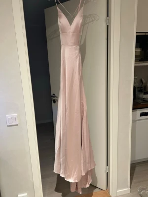 Ljusrosa balklänning - Helt oanvänd, kommer i originalförpackningen & påsen. Ljusrosa balklänning i satin material. Klänningen har öppen rygg med snygg snörning och ett fint ”släp”. Ordinare pris 4500kr men tar bud med 