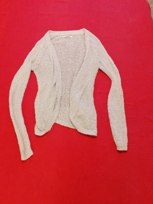 Beige stickad öppen kofta - Mysig beige stickad kofta med öppen front och långa ärmar. Koftan har en avslappnad passform och är tillverkad i ett mjukt, strukturerat material som passar perfekt för lager på lager. Enkel och stilren design som är lätt att matcha.