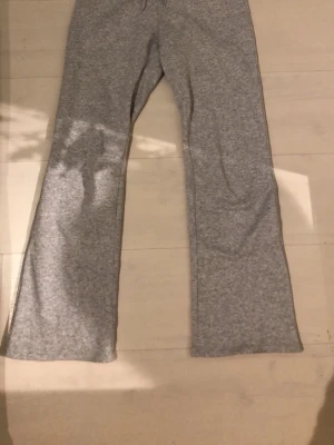 Grå mjukisbyxor med utsvängda ben - Säljer ett par ljusgrå mjukisbyxor med utsvängda ben och dragsko i midjan. Byxorna är tillverkade i mjukt sweatshirtmaterial och har en avslappnad passform. Perfekta för chill dagar eller när du vill vara extra bekväm.