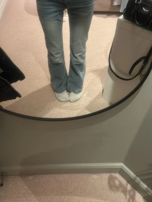 Ljusblå bootcut jeans med fickdetalj - Säljer ett par ljusblå bootcut jeans med klassisk femficksmodell och knappdetalj på bakfickan. Jeansen har hög midja och är tillverkade i denim med lätt tvättad look. Perfekta för dig som gillar en avslappnad men trendig stil.