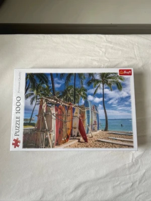 Pussel 1000-bitar - Ett oanvänt plastat pussel som föreställer färgglada surfbrädor på Waikiki Beach, Hawaii. Pusslet mäter 68,3 x 48 cm när det är färdigt och har en härlig strandbild med palmer och blå himmel.