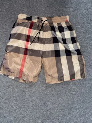 Burberry badbyxor  - Snygga badbyxor från Burberry med klassiskt beige, svart, vitt och rött rutmönster. 
