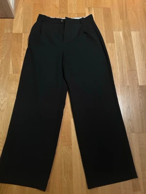 Svarta vida kostymbyxor - Säljer ett par svarta kostymbyxor med hög midja och vida ben. Byxorna har hällor för skärp och diskreta sidofickor. Perfekta för en clean och stilren look. Materialet känns mjukt och följsamt.