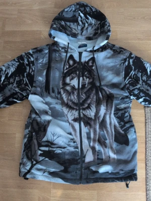 Grå hoodie med vargmotiv från Walk - Säljer en grå och svart hoodie från Walk Outdoor med ett stort, detaljerat vargmotiv på framsidan och baksidan. Hoodien har dragkedja, huva och är gjord i mjuk fleece. Perfekt för dig som gillar djurmotiv och vill ha något riktigt unikt i garderoben. Passar bra att ha som vår jacka eller kanske till och med vinter. 