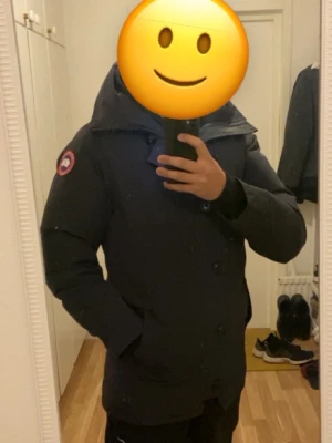 Svart dunjacka Canada Goose M (kvitto finns) - Säljer en svart Canada Goose Chateau i storlek M. Jackan har huva, klassisk logga på ärmen, dragkedja och knappar framtill. Perfekt för kalla dagar med sin dunfyllning och stilrena look. Passar dig som vill ha en varm och snygg vinter jacka. Kvitto finns tillgängligt.