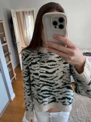 Stickad tröja med zebramönster - Säljer en fluffig stickad tröja med zebramönster i vitt och mörkgrönt. Tröjan har rund hals, ribbade muddar och avslut. Säljer bara för att den inte komemr till användning!