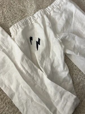 Vita linnebyxor med blixtdetalj - Säljer ett par vita linnebyxor med resår i midjan och dragsko. Byxorna har blixtar som detalj på baksidan. tunt tyg som känns luftigt. 