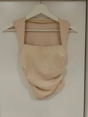 Beige ribbad ärmlös topp - Beige/creamefärgad topp i ribbat material med breda axelband och fyrkantig ringning. Toppen är ärmlös och har en croppad passform. Aldrig använd 