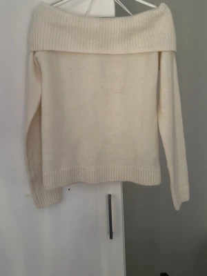 Off shoulder cremefärgad stickad tröja - Trendig cremefärgad stickad tröja med off shoulder-design och bred ribbad kant upptill. Långa ärmar och ribbade muddar vid ärmslut och nederkant. Perfekt för dig som vill ha en stilren och mysig look. Helt oanvänd 