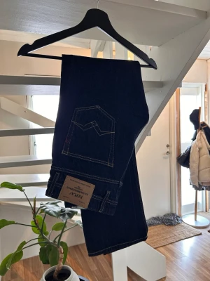 Helt nya Mörkblå replay Jeans - Säljer ett par mörkblå jeans från replay  med klassisk femficksmodell och raka ben. Jeansen har kontrastsömmar och är tillverkade i kraftig denim. Perfekta för dig som gillar en stilren och tidlös look.