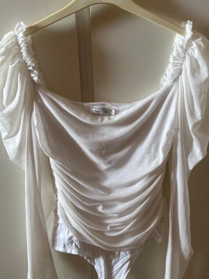 Vit offshoulder body från NLY One - Vit body från nelly med långa puffärmar och rynkade detaljer framtill. Tillverkad i ett tunt, lätt material som ger en romantisk vibe. Plagget är i bra skick 